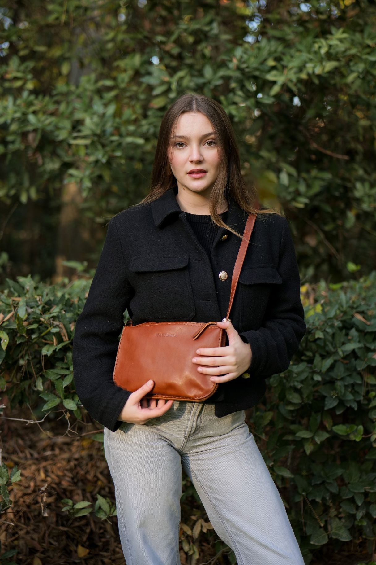 Femme portant le sac bandoulière en cuir châtaigne Noordsen N003-06 à l'épaule.