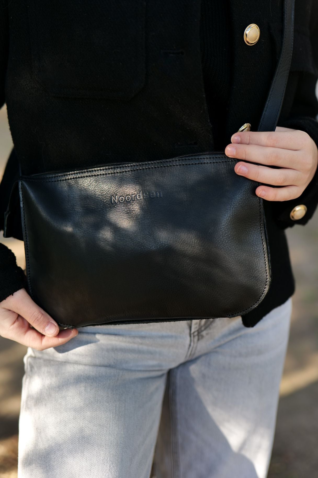 Détail du sac bandoulière en cuir noir Noordsen N003-06 à l'épaule.